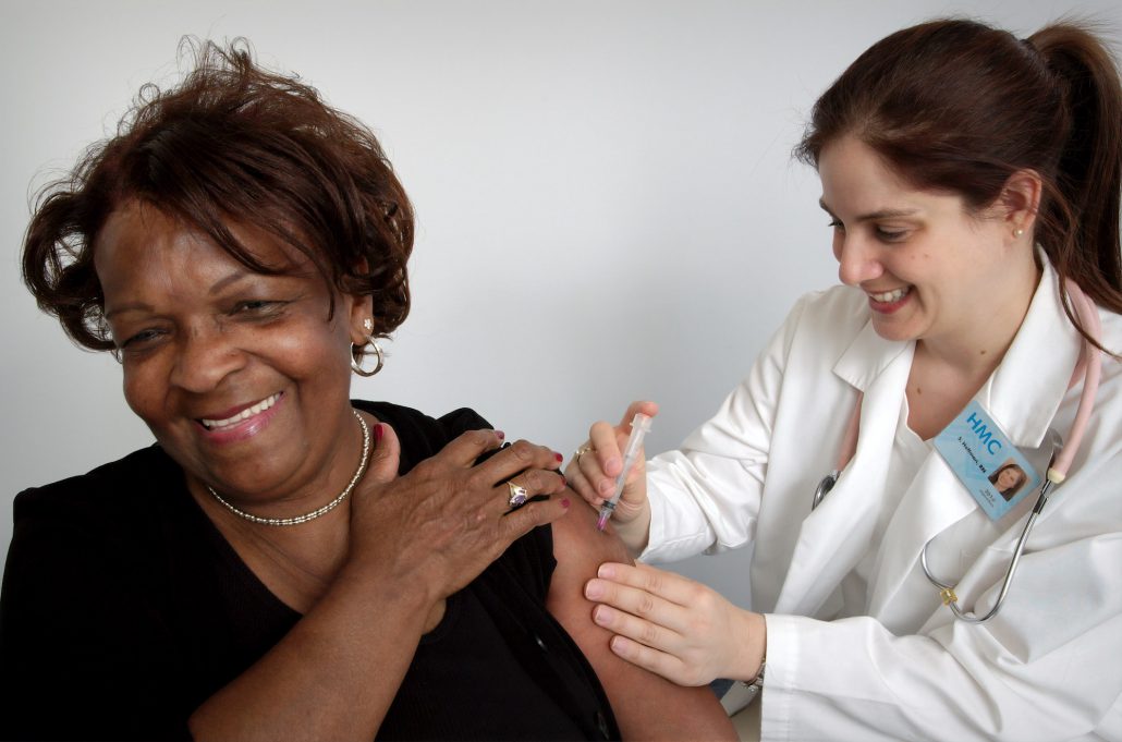 Happy Black Woman patient getting a shot administrated by a happy Woman doctor