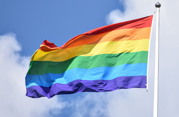 Rainbow pride flag blowing in wind under cloudy sky