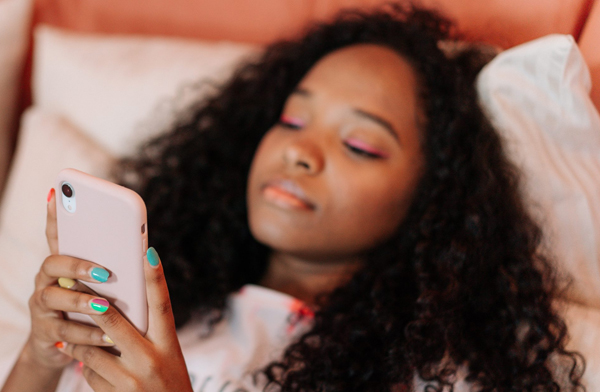 Young black woman looking at cellphone in bed