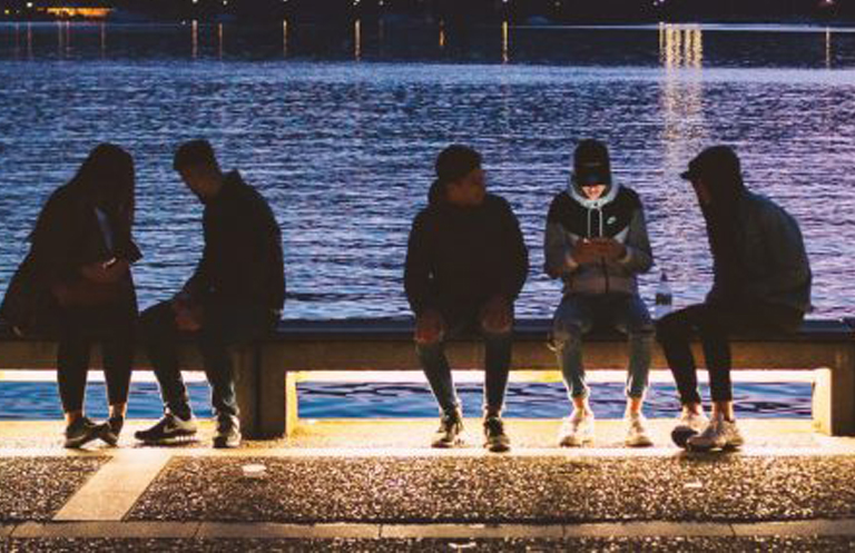 Silhouette of five gen z people sitting on park bench