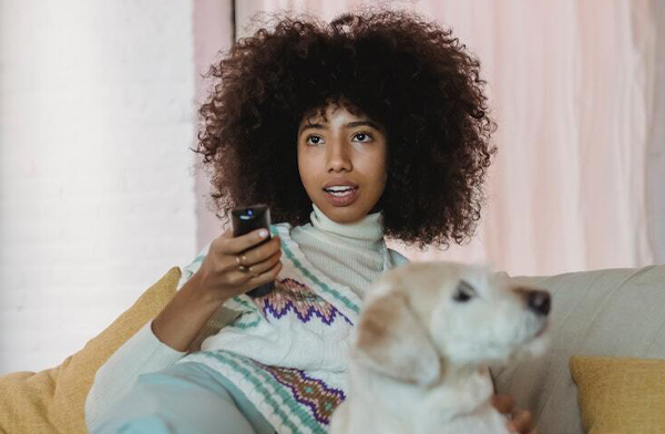 young black woman watching tv with white dog
