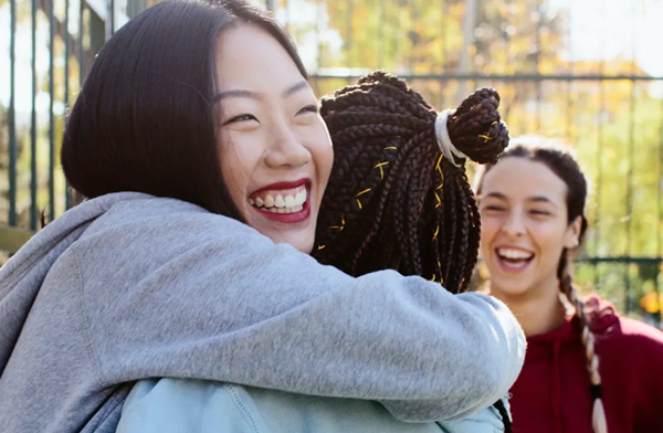 Asian women smiling and hugging black woman with braids