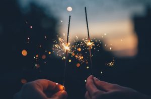 Two people's hands holding sparklers at dusk