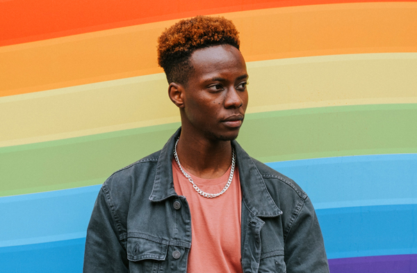 Contemplative black man standing in front of LGBTQ pride flag