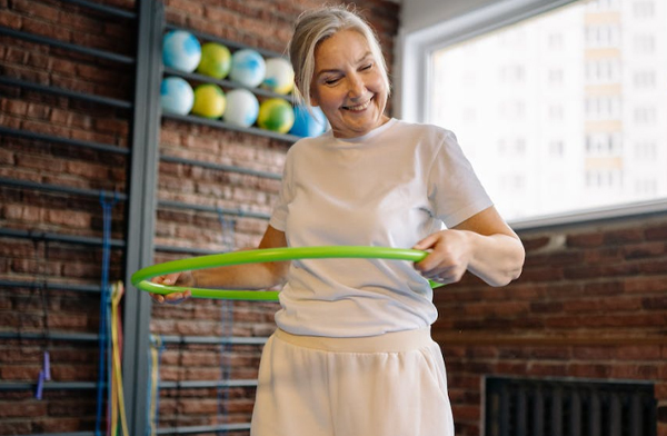 Grey haired woman exercising with a green hula hoop