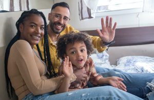Multiracial couple waving at camera with their daughter