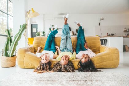 Three Gen Z Hispanic women laughing together on a couch