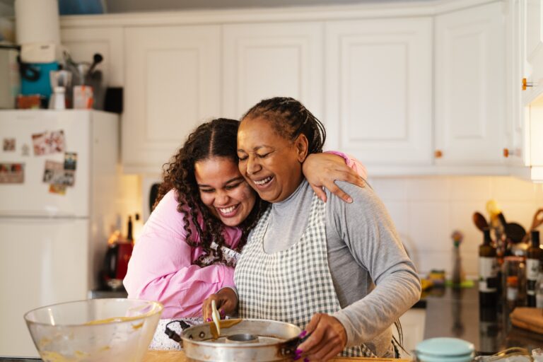 Black mother and daughter smiling while embracing and cooking together