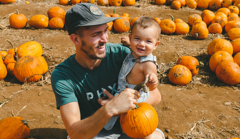 Young Gen Z man holding a toddler on his lap in a pumpkin patch