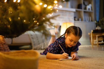 Little girl writing Christmas list under tree