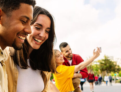 Young adult friends using mobile phone together outside. Gen Z people generation having fun watching social media content on cell. Youth and technology concept