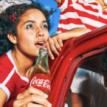 Two people in car smiling holding coca-cola bottle