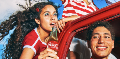 Two people in car smiling holding coca-cola bottle