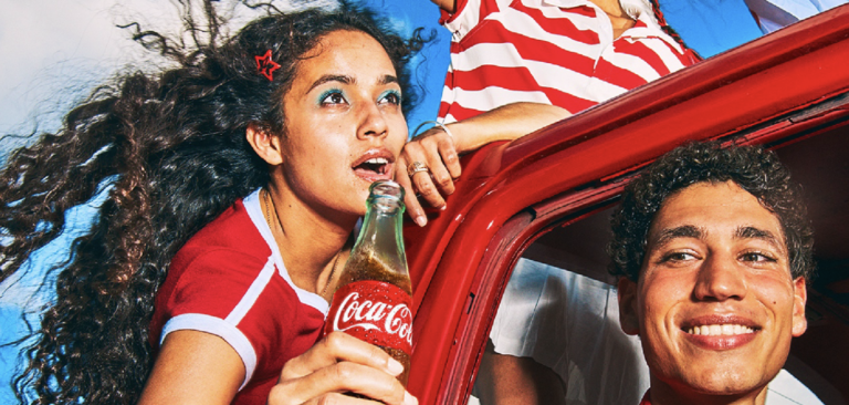 Two people in car smiling holding coca-cola bottle