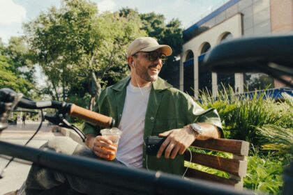 Hispanic man holding a coffee and sitting on a park bench