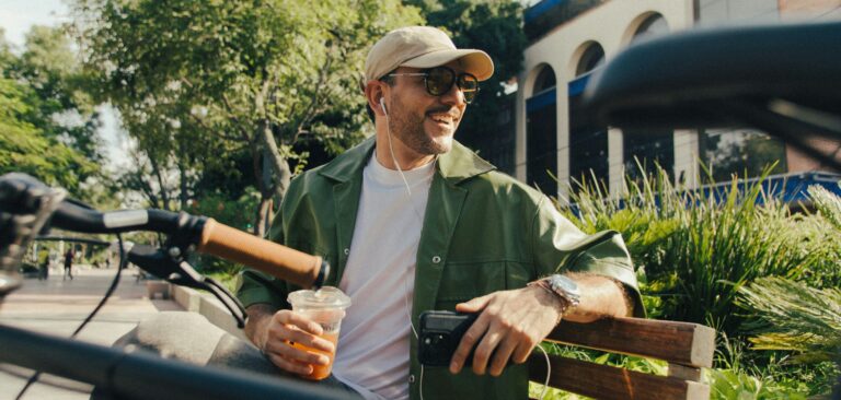 Hispanic man holding a coffee and sitting on a park bench
