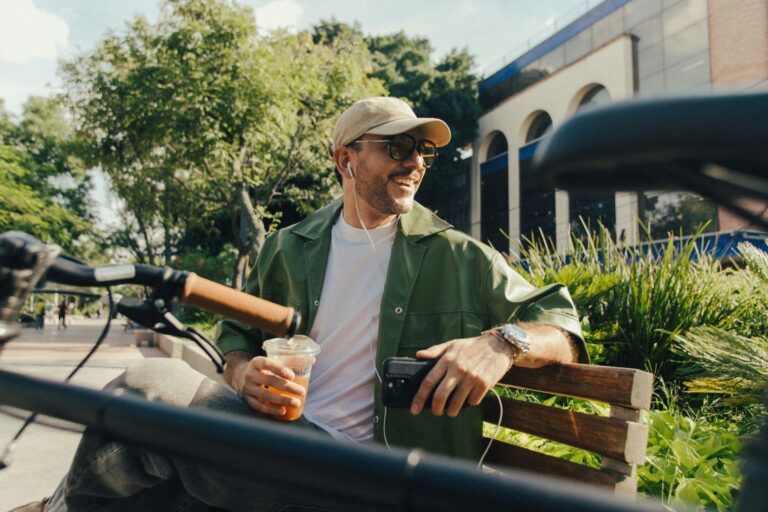 Hispanic man holding a coffee and sitting on a park bench