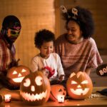 Family dressed up for Halloween with carved, lit up pumpkins on the table in front of them
