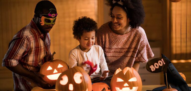 Family dressed up for Halloween with carved, lit up pumpkins on the table in front of them